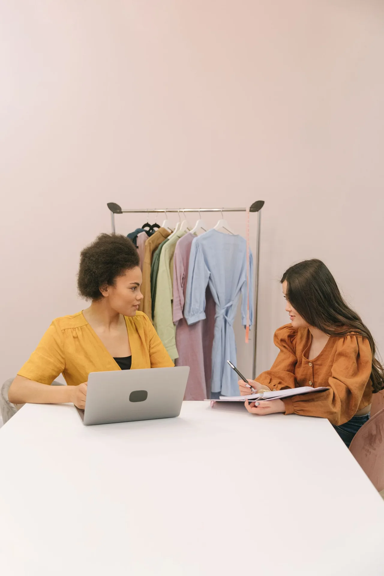 Two women discussing paperwork beside a laptop in a shop workspace. Illustrative stock photograph.